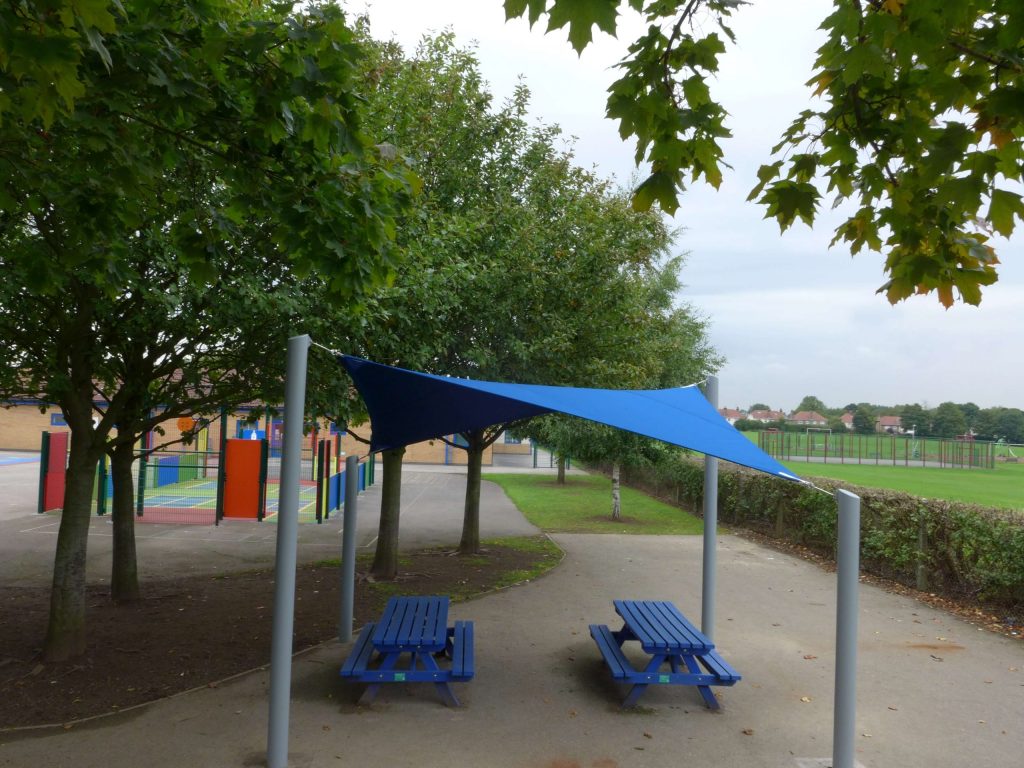 Triangular blue sail shade over picnic benches