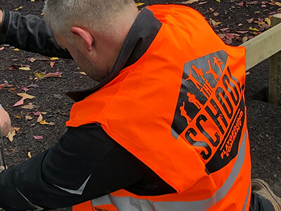 Repair worker for school playgrounds wearing orange 'The School Playground Company' safety vest