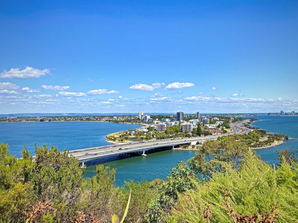 A build area of city on a small green area of land in a large body of water with a large highway built through the centre and over the water