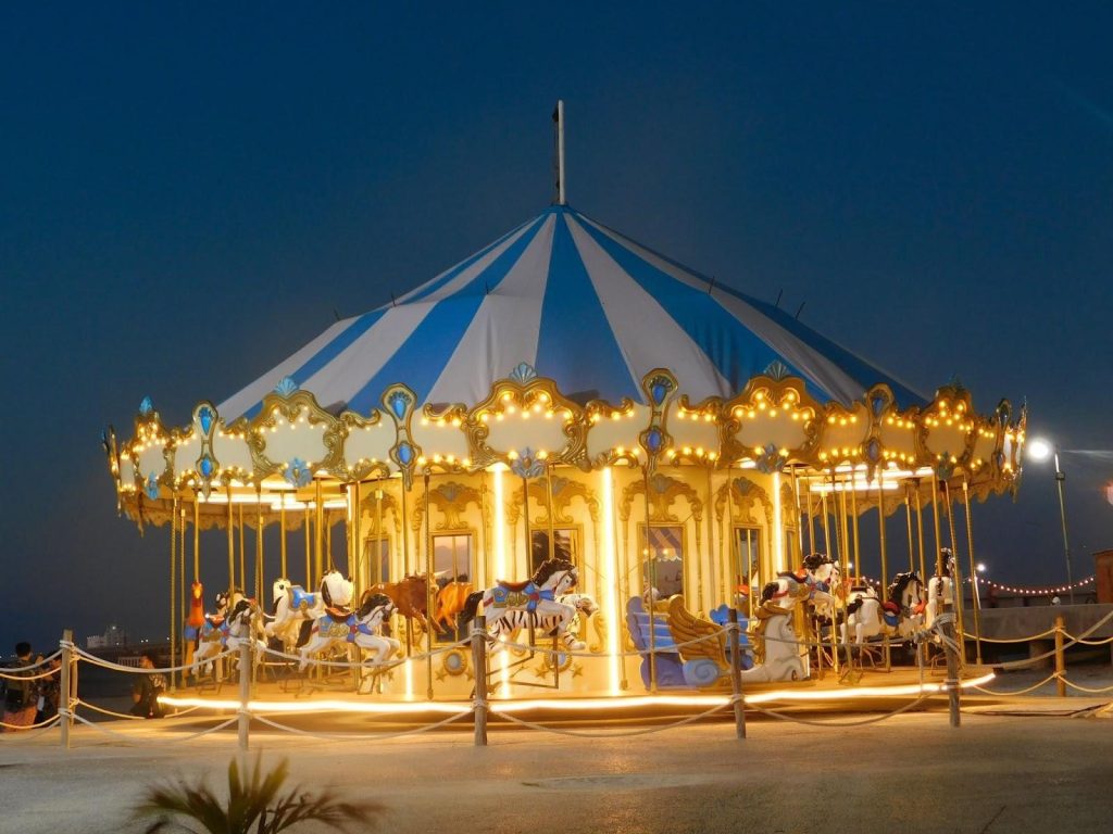 A lit-up merry-go round with a blue and white striped roof