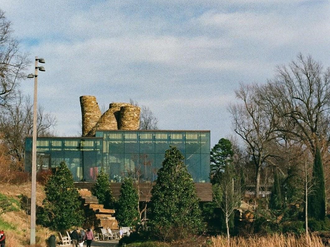 A modern glass and wood building with old-fashioned stone towers located in a green wooded area