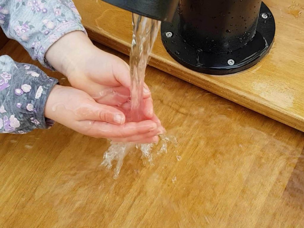 Photograph of a young child’s hands under the running water of a wooden water play table from our sensory playground equipment range