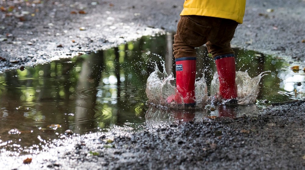 A child enjoying splashing in a muddy puddle in red welly-boots and yellow rain coat
