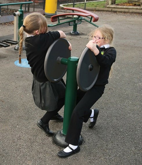 Two children using the Double Strength Challenge Dual Outdoor Gym Equipment for kids. They each try to spin connected disks in opposite directions from one another as a fun and collaborative test of strength.