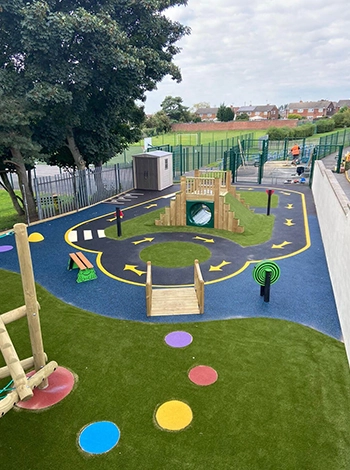 School Playground with artificial grass and vibrant playground markings and a wetpour rubber racetrack design around a large wooden play structure with artificial grass slanted walls