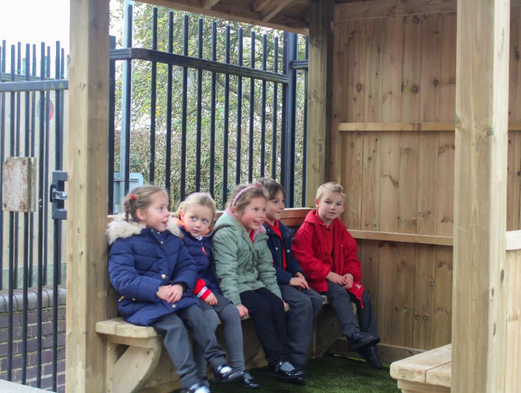children seated on bench inside square wooden gazebo