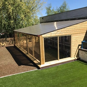 Wooden outdoor classroom shelter with floor to ceiling windows and slanted roof