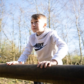 Child climbing up a timber log on an active play structure
