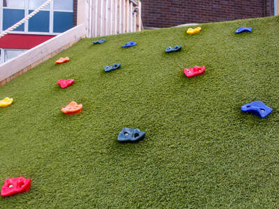 artificial grass climbing slope with plastic hand holds in a Warwickshire School Playground