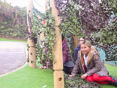 Den making playground set with children underneath leaf canopy netting on wooden tree trunk poles