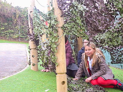 Den making creative playground set in Nottinghamshire School Playground with children underneath leaf canopy netting on wooden tree trunk poles