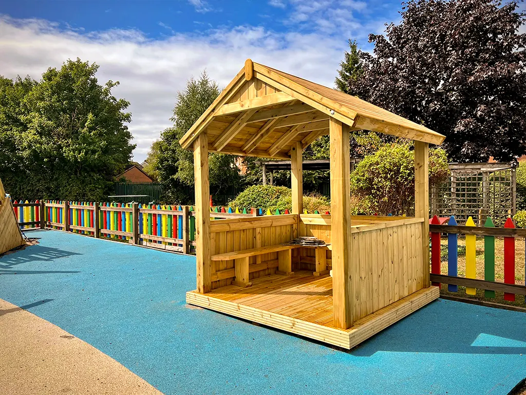 An outdoor wooden play house gazebo with open sides and benches inside