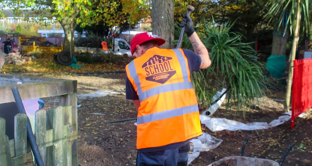 Workman in orange School Playground Company fluorescent vest digging on a playground site