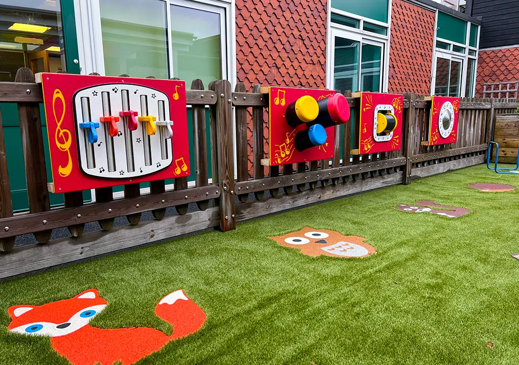 Music set play panels on fence with animal-themed playground markings on play grass