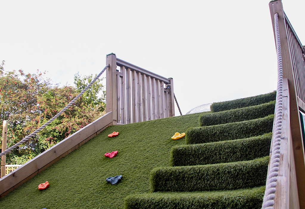 Grass carpeted climbing slope with hand holdsand stairs