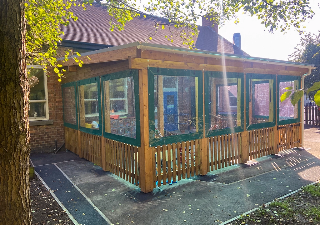 wooden outdoor classroom shelter with windows adjoining a school building
