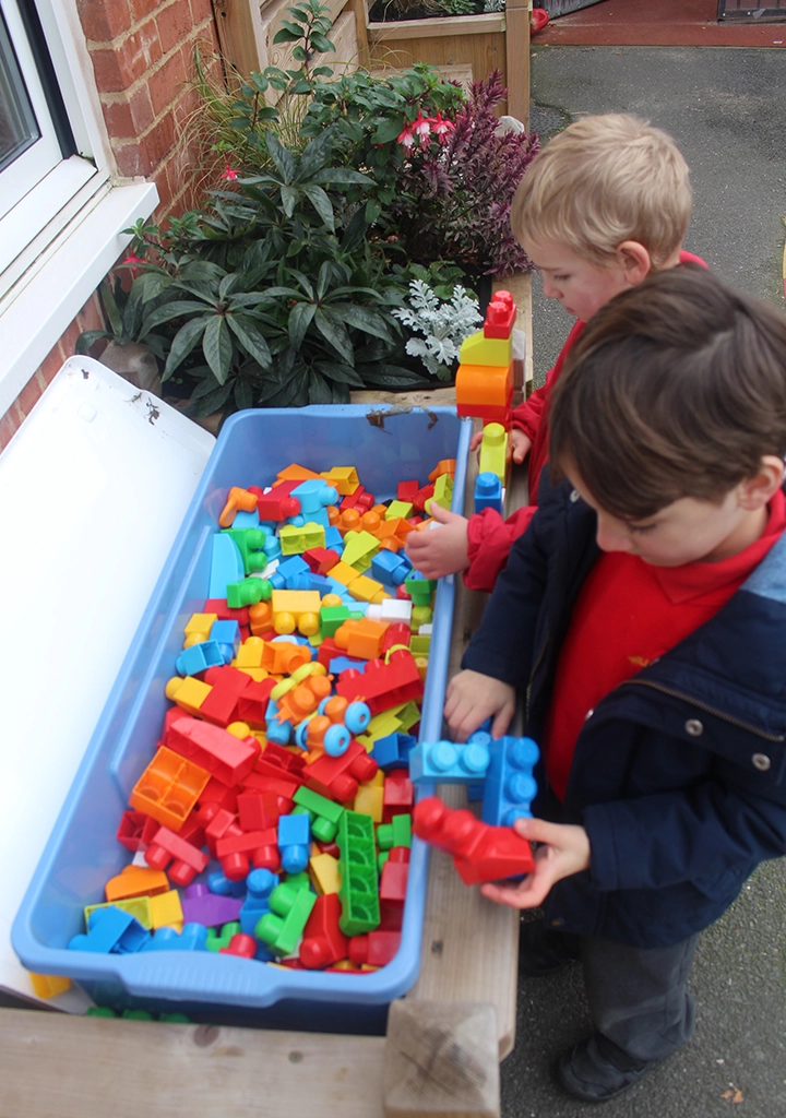 Children playing with sensory blocks on a wooden outdoor side table in a Nottinghamshire school playground