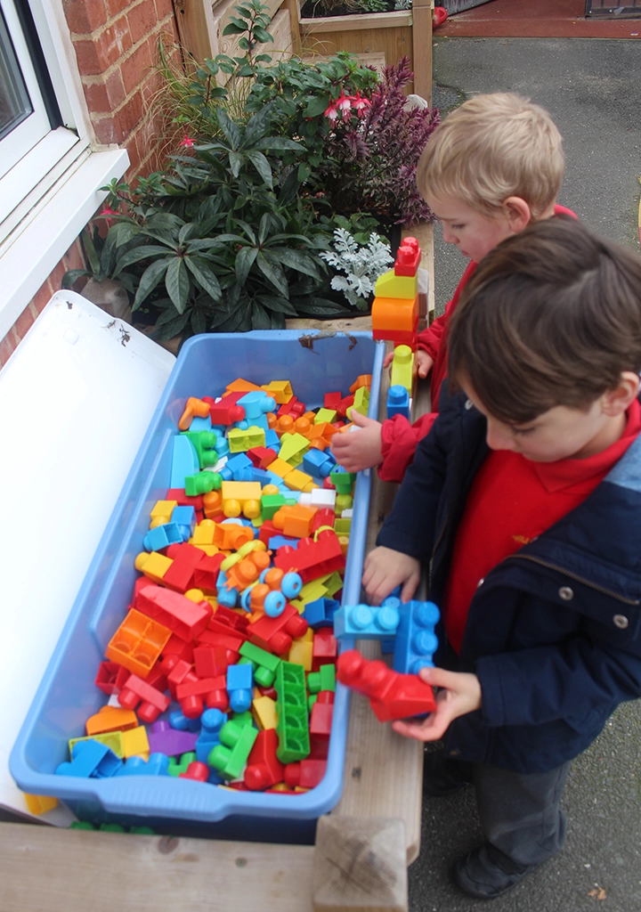 Young children playing with sensory block toys on an outdoor table bench