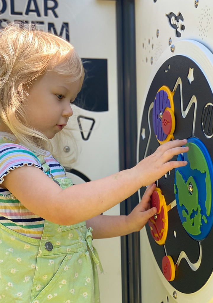 Inclusive outdoor play panel with a solar system theme being used by a child