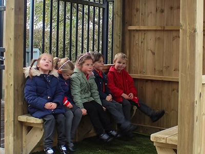 children inside a square wooden play house gazebo with artificial grass interior and benches in a Nottinghamshire school playground