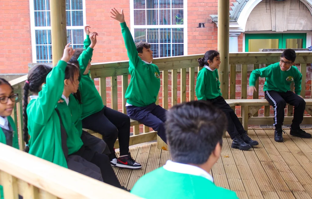 Children in a lesson in a large outdoor classroom wooden school gazebo with wooden benches in a Nottinghamshire school playground