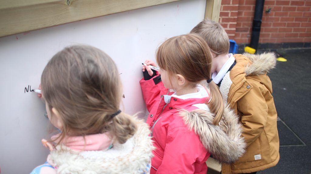Children writing on a freestanding whiteboard mark making panel
