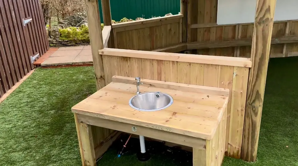 A sink attached to the exterior of a large outdoor classroom gazebo.