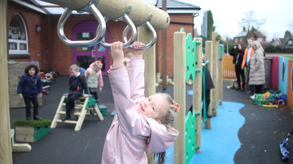 Child dangling from the climbing elements of their trim trail