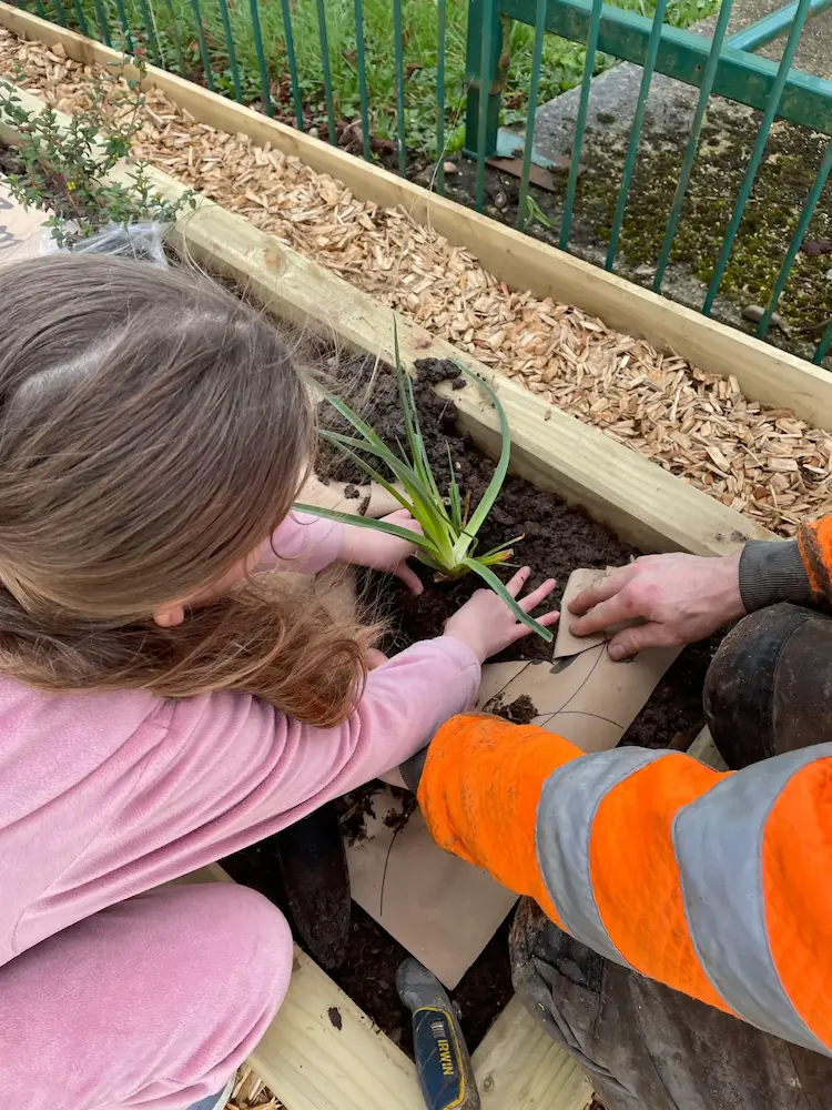 A child and an adult nurturing a plant in a planter.