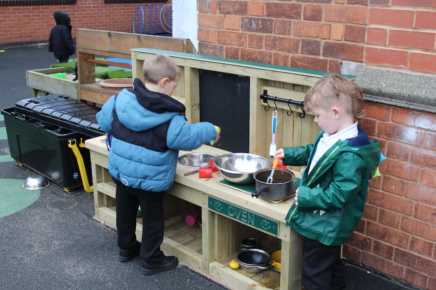 Two EYFS Children using the Mud Kitchen