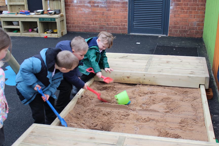Three EYFS Children using the Sand Pit