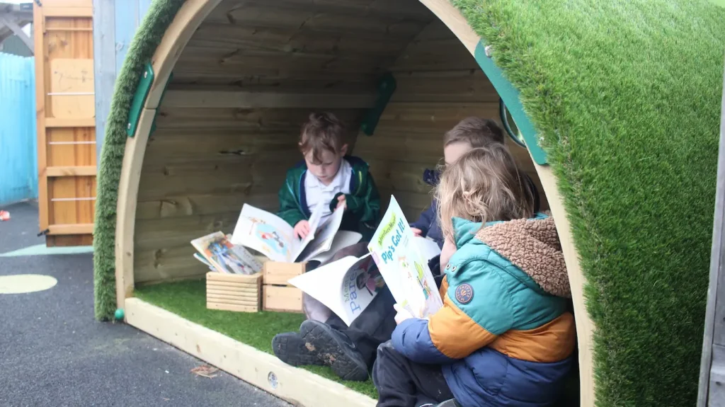 children reading in hobbit house den. Small open semi circle shelter with artificial grass carpet