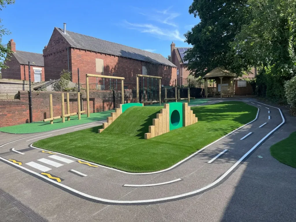 school playground trim trail with grass mound, tunnel and road markings
