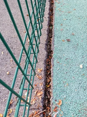 deteriorated edging strip with debris trapped between tarmac and rubber mulch