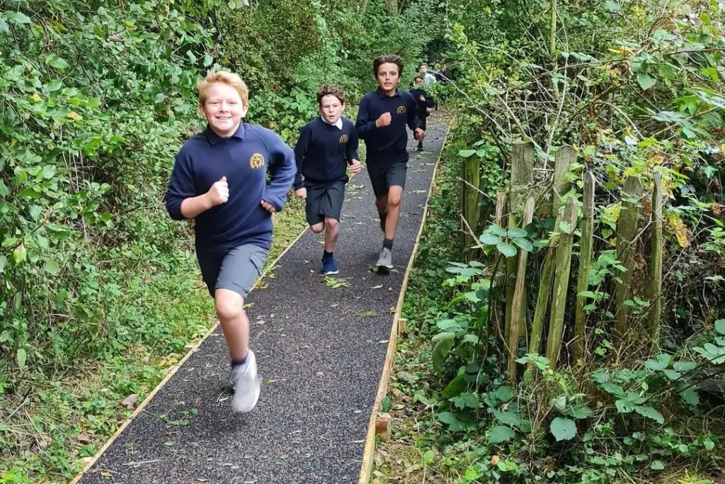 Playground Surfacing | Daily Mile Track Children running the Daily Mile on a running track through a wooded area in an Oxfordshire school sports and play area