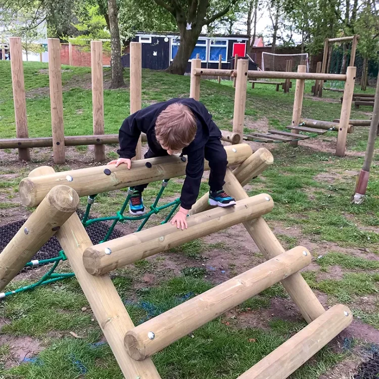 A child climbing over a wooden A-Frame Trim Trail climbing component