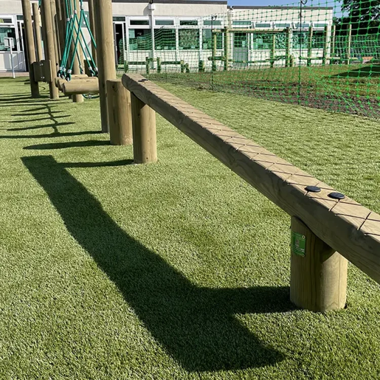 Wooden balance beam positioned low to the ground with criss-crossed markings for slip-resistance