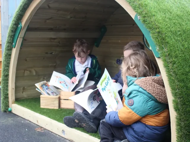 children reading in hobbit house den. Small open semi circle shelter with artificial grass carpet