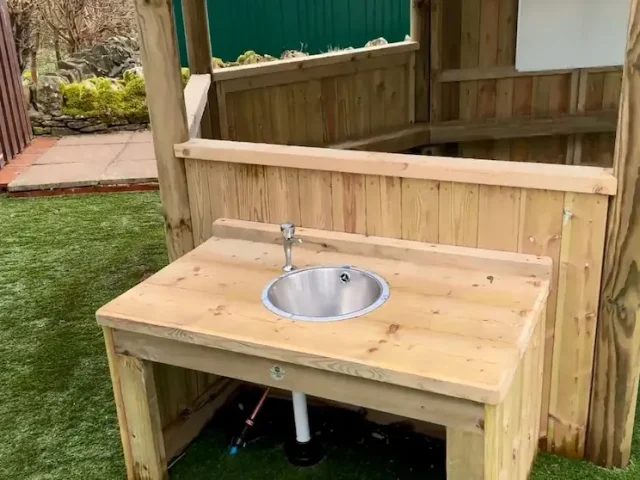 A sink attached to the exterior of a large outdoor classroom gazebo.