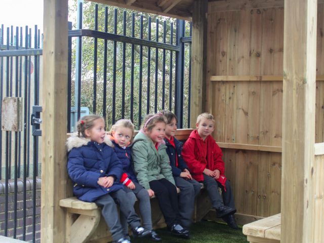 children seated on bench inside square wooden gazebo