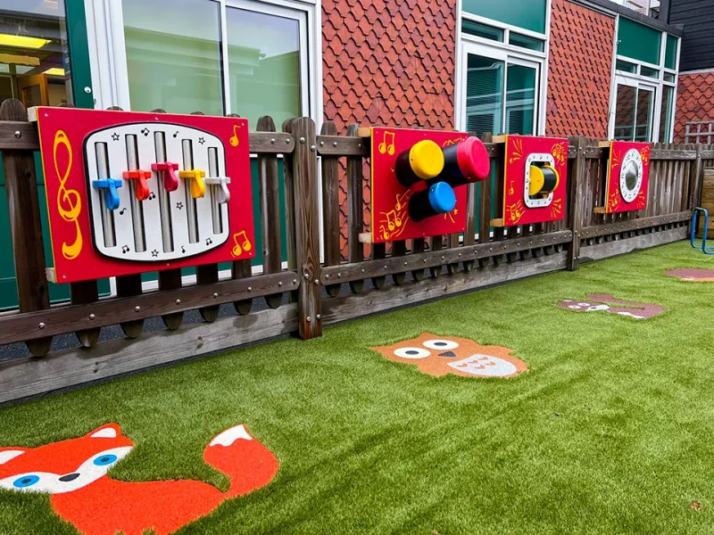 Music set play panels on fence with animal-themed playground markings on play grass