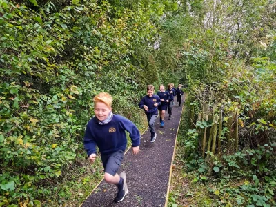 Children running on a daily mile running track through a wooded area in an Oxfordshire school sports and play area